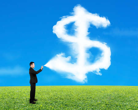 Businessman spraying dollar sign shape cloud paint with sky grass backgroundの写真素材