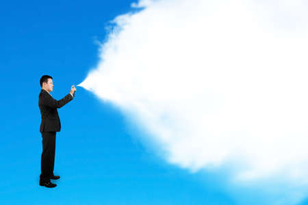 Business man spraying white cloud paint isolated on blue backgroundの写真素材