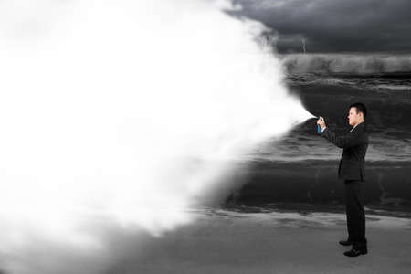 Business man spraying white cloud paint covered dark stormy ocean backgroundの写真素材