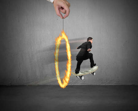 Businessman skating on money skateboard through fire circle with concrete room backgroundの写真素材
