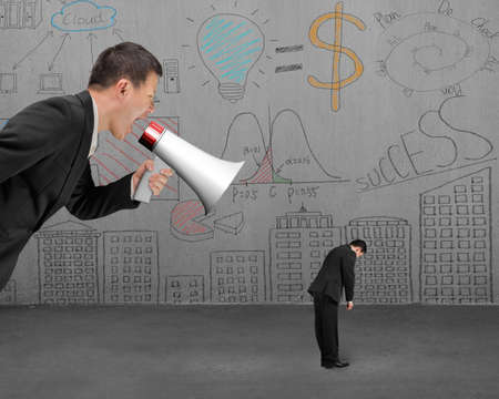 Businessman using megaphone yelling at his employee with doodles wall backgroundの写真素材