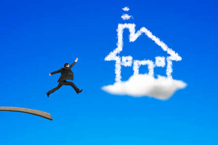 Businessman jumping from wooden board to house shape cloud with blue sky backgroundの写真素材
