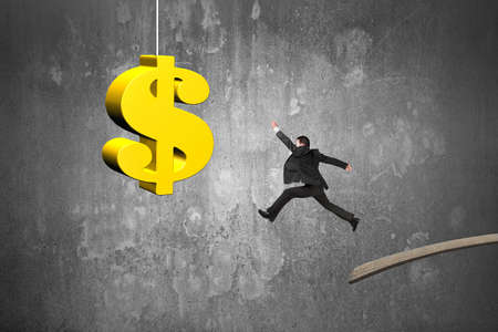 Businessman jumping from wooden board to golden dollar sign with concrete wall backgroundの写真素材