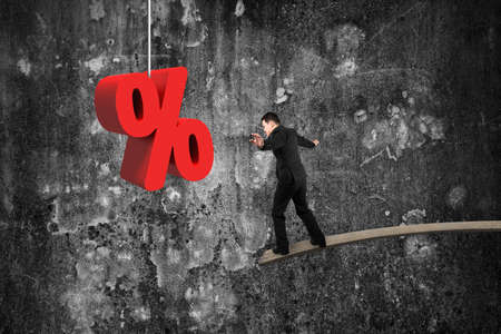 Businessman balancing on wooden board with red percentage sign and mottled concrete wall backgroundの写真素材
