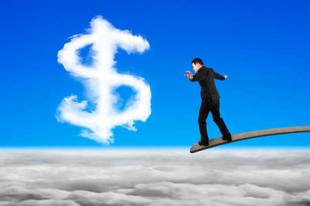 Businessman balancing on wooden board with dollar sign shape cloud on sky cloudscape backgroundの写真素材