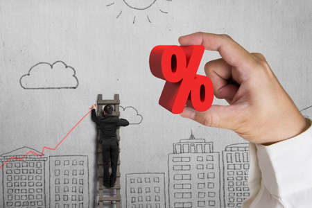 Hand holding 3D red percentage sign with businessman drawing trend chart on doodles wall backgroundの写真素材