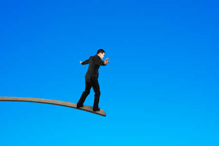 Businessman balancing on wooden board with blue sky background