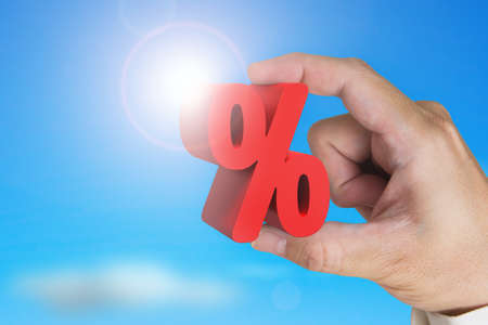Hand holding 3D red percentage sign with sky sunlight backgroundの写真素材