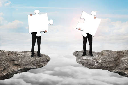Businessmen holding two white jigsaw puzzles to connect on the cliff with cloudscape sunlight...