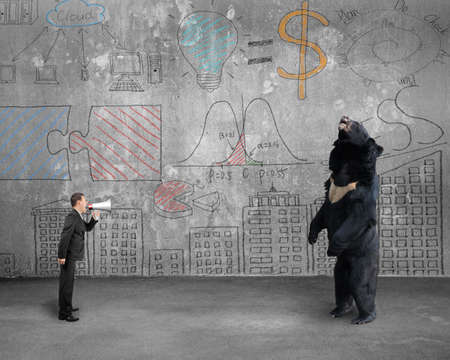 Businessman using megaphone yelling at black bear with business concept doodles wall backgroundの写真素材