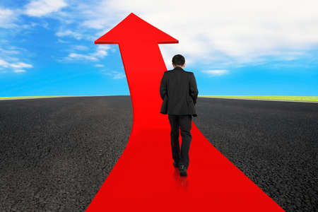 Businessman walking on red arrow up road with asphalt pavement and sky clouds backgroundの写真素材