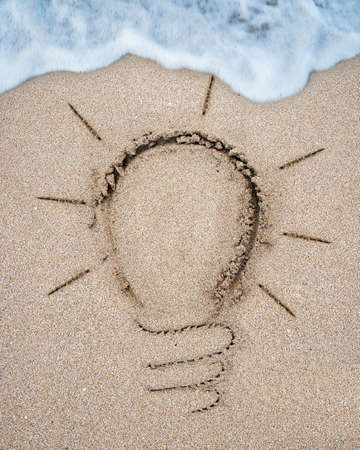 Image of light bulb drawn on the sand beach with white wave foam backgroundの写真素材