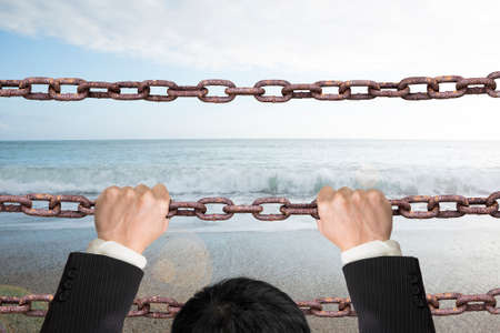Businessman climbing on old iron chains to go out with natural sky sea background