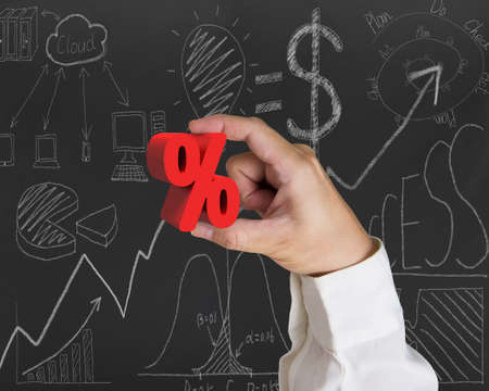 Hand holding 3D red percentage sign with business concept doodles blackboard backgroundの写真素材