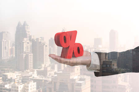 Glass reflection of hand showing 3D red percentage sign with city buildings backgroundの写真素材