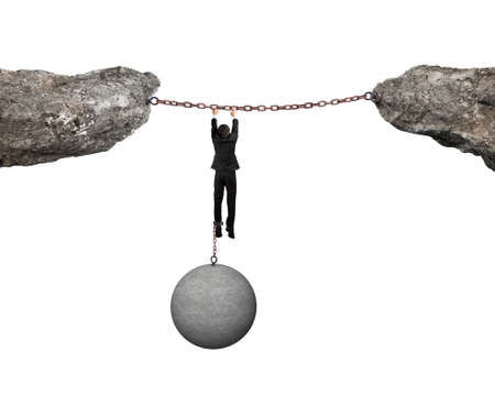 Businessman shackled by heavy concrete ball hanging on iron chains connected two cliffs with white backgroundの写真素材