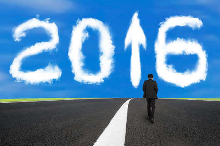 Businessman walking on asphalt road with separation white line and 2016 year arrow up sign shape clouds in the blue skyの写真素材