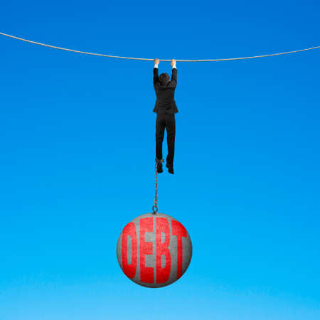 Businessman shackled by debt concrete ball hanging on the rope with blue backgroundの写真素材