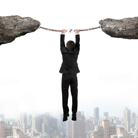 Businessman hand hanging on the broken rusty iron chains connect two cliffs with urban scene skyline backgroundの写真素材