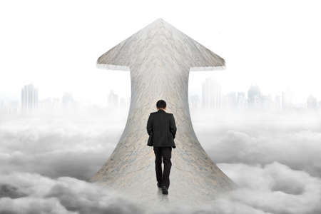 Black suit businessman walking on arrow up sign marble road with cloudy cityscape backgroundの写真素材