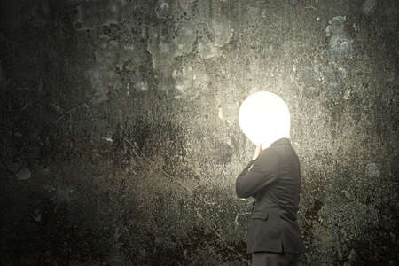 Thinking businessman with lamp head illuminated the dark mottled concrete wall backgroundの写真素材