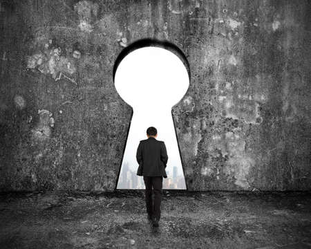 Businessman walking toward keyhole door with city buildings view on mottled concrete wall backgroundの写真素材