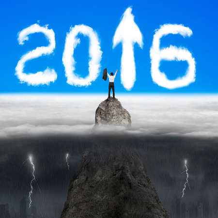 Businessman cheering on mountain peak for white 2016 year arrow up sign shape clouds in the sky with...