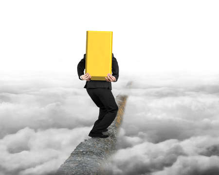 Businessman carrying big 3D gold bullion balancing on concrete ridge with gray cloudy sky background