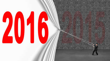 Businessman pulling down 2016 curtain covering old 2016 brick wall on gray concrete floorの写真素材