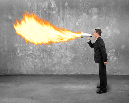 Angry businessman screaming into megaphone spitting fire flame with concrete indoor backgroundの写真素材