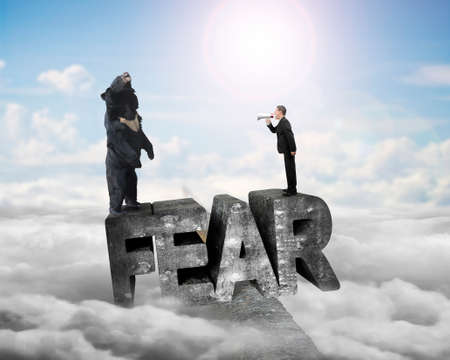 Businessman using megaphone yelling black bear at 3D mottled concrete fear word, balancing on ridge with sky sunlight cloudscape backgroundの写真素材