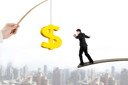 Man balancing on wood board for 3D golden dollar sign bait from fishing rod hand holding with urban scene backgroundの写真素材