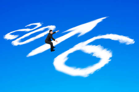 Man riding white 2016 year arrow up sign shape clouds with raised finger pointing direction on blue sky backgroundの写真素材