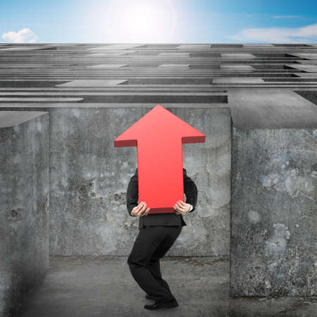 Man carrying big 3D red arrow up sign entering the huge maze with blue sky clouds backgroundの写真素材