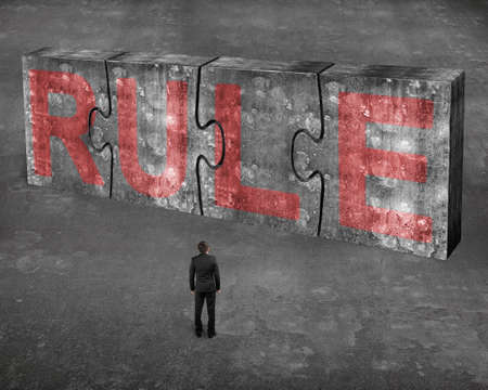 Businessman facing red rule word on four huge concrete puzzles connected together, on gray cement floor backgroundの写真素材