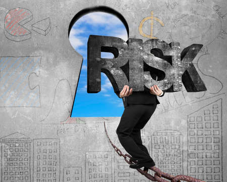 Man carrying big 3D RISK concrete word walking on old iron chain toward keyhole door, with sky...