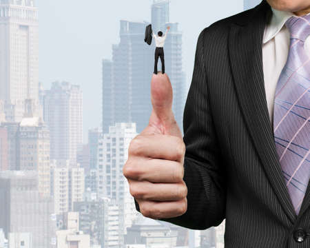 Business man cheering on top of another big thumb with city buildings backgroundの写真素材