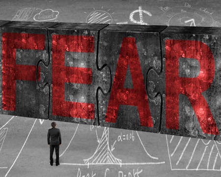 Businessman facing red fear word on four huge concrete puzzles connected together, with business concept doodles backgroundの写真素材