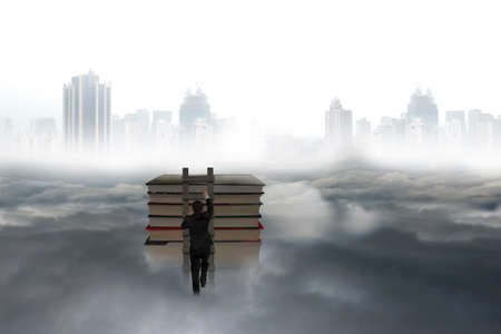 Business man climbing on wooden ladder to top of books with city landscape gray cloudscape backgroundの写真素材