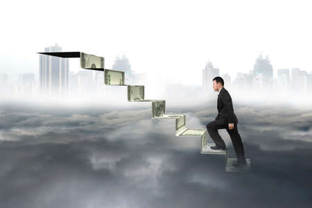 Man climbing on money stairs with city landscape gray cloudscape backgroundの写真素材