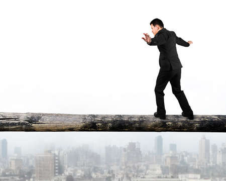 Businessman walking on the tree trunk high in the sky, with cityscape background.の写真素材