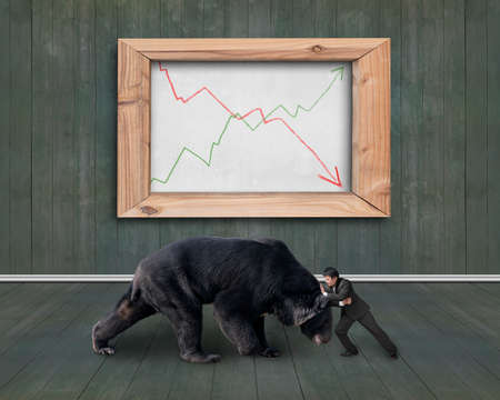 Businessman fighting against black bear with two trend lines of whiteboard, on wooden indoors...