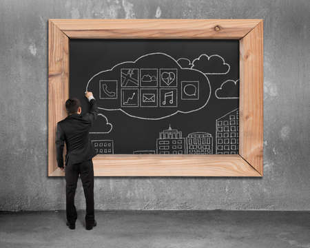 Businessman drawing app icons on blackboard with concrete wall and floor backgroundの写真素材
