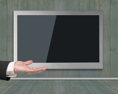 Blank black wide flat TV screen hanging on wooden wall, with human hand open palm upwards.