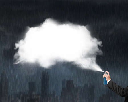 Male hand spraying white cloud paint on heavy rain dark cityscape backgroundの写真素材