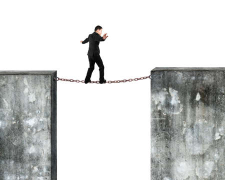 Businessman balancing on rusty chain connected two high dirty concrete walls, with white background.の写真素材