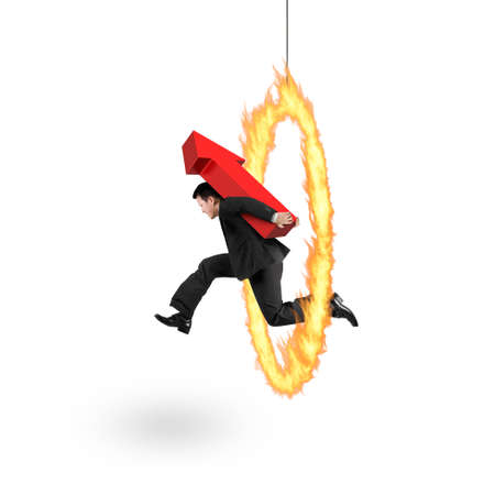 Businessman carrying 3D red arrow up sign, jumping through fire hoop, isolated on white background.の写真素材