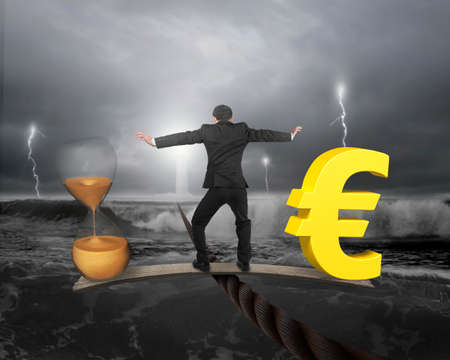 Man standing on wood board between hourglass and golden euro sign, balancing on wire, with dark stormy ocean background. Time is money concept.の写真素材