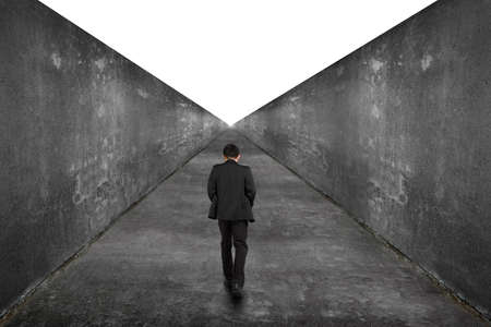 Businessman walking on one way road toward the exit of blank white view, with high dirty concrete...