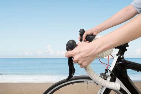 Closeup on woman hands riding a bike, with blue sky sea beach background.の写真素材